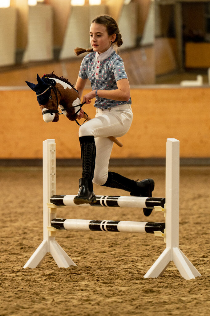 Mädchen springt konzentriert mit Hobby Horse über Sprung auf einem Hobby Horsing Turnier
