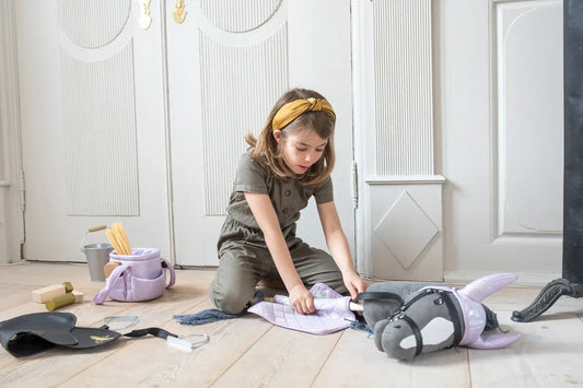 Mädchen mit grauem Hobby Horse spielt mit Decke und Fliegenhaube im Wohnzimmer