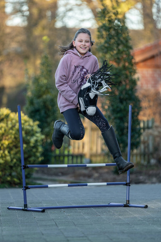 Mädchen springt freudig über Hobby Horsing Sprung