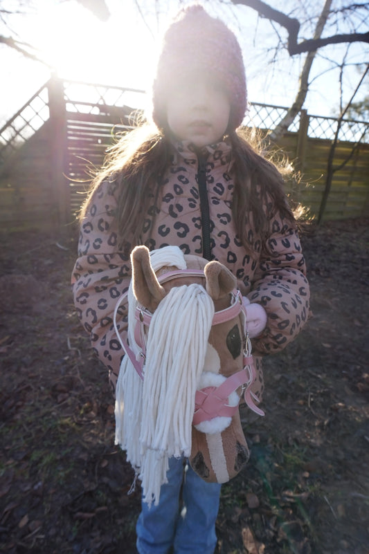 Hobby Horse mit mexikanischem Reithalfter in rosa in der Morgensonne in einem Garten