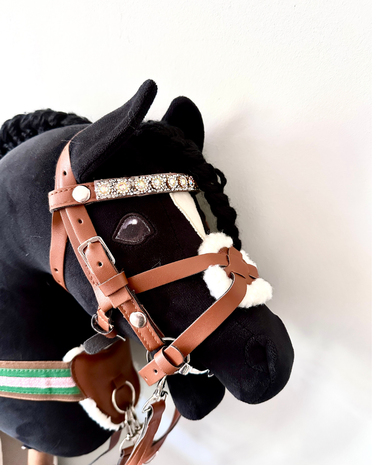 schwarzes Hobby horse, welches panduro hobby horse trense in braun mit passendem vorderzeug und glitzerstirnriemen präsentiert