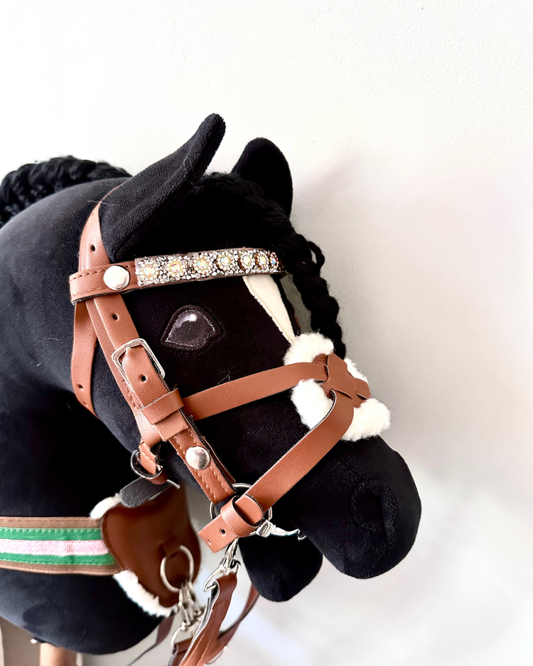 schwarzes Hobby horse, welches panduro hobby horse trense in braun mit passendem vorderzeug und glitzerstirnriemen präsentiert