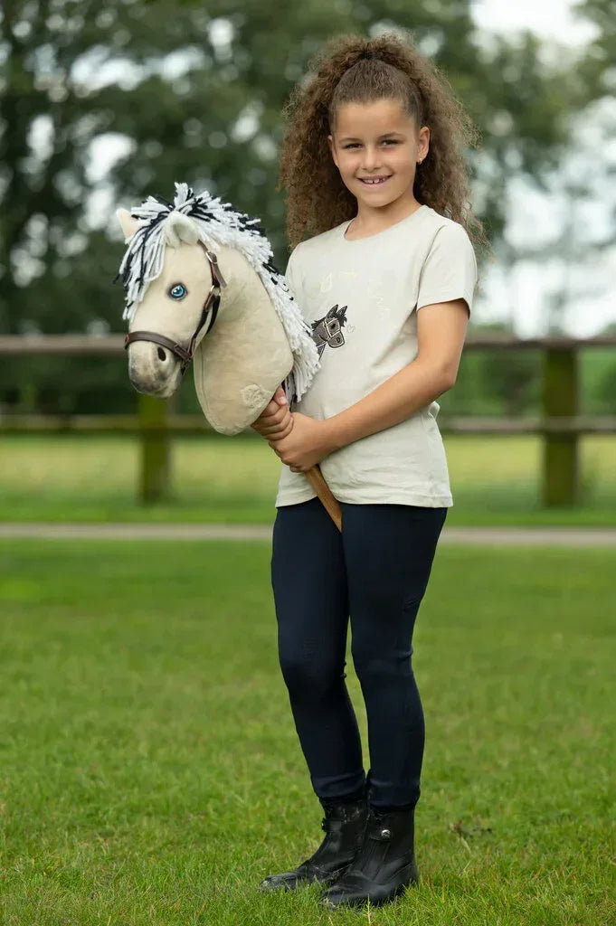 Ein Mädchen steht mit einer Norweger Hobby Horse auf einer Wiese. Das Hobby horse trägt ein braunes Halfter. 