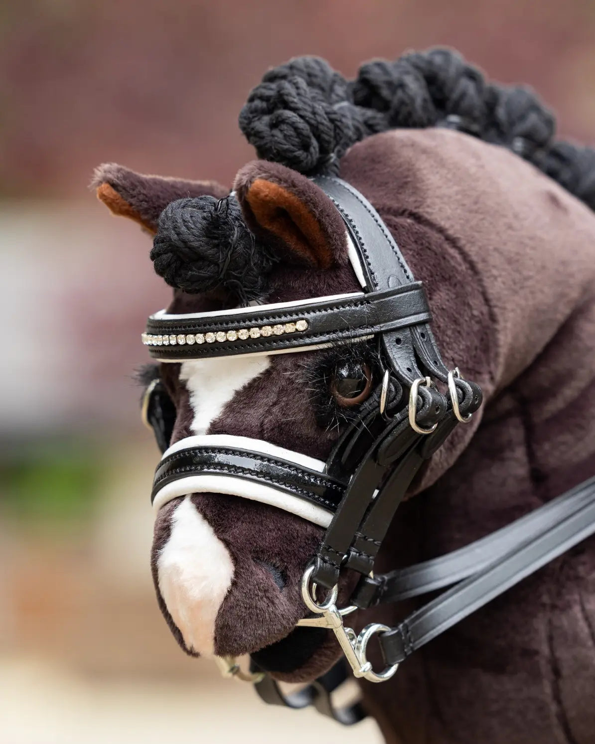 Turnierzubehör für Hobby Horsing: Detailansicht der LeMieux S-Klasse Dressurkandare aus schwarzem Lackleder an einem dunkelbraunen Plüsch-Steckenpferd.
