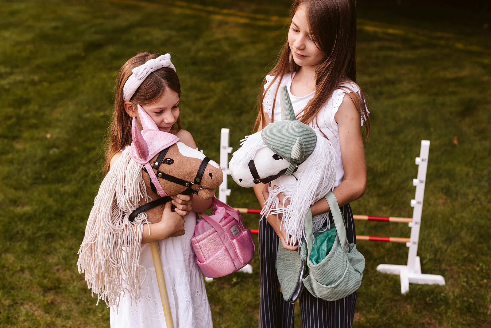 Mädchen seht mit einer Putztasche Hobby Horsing in rosa auf einer Wiese und hat ein Hobby Horse im Arm