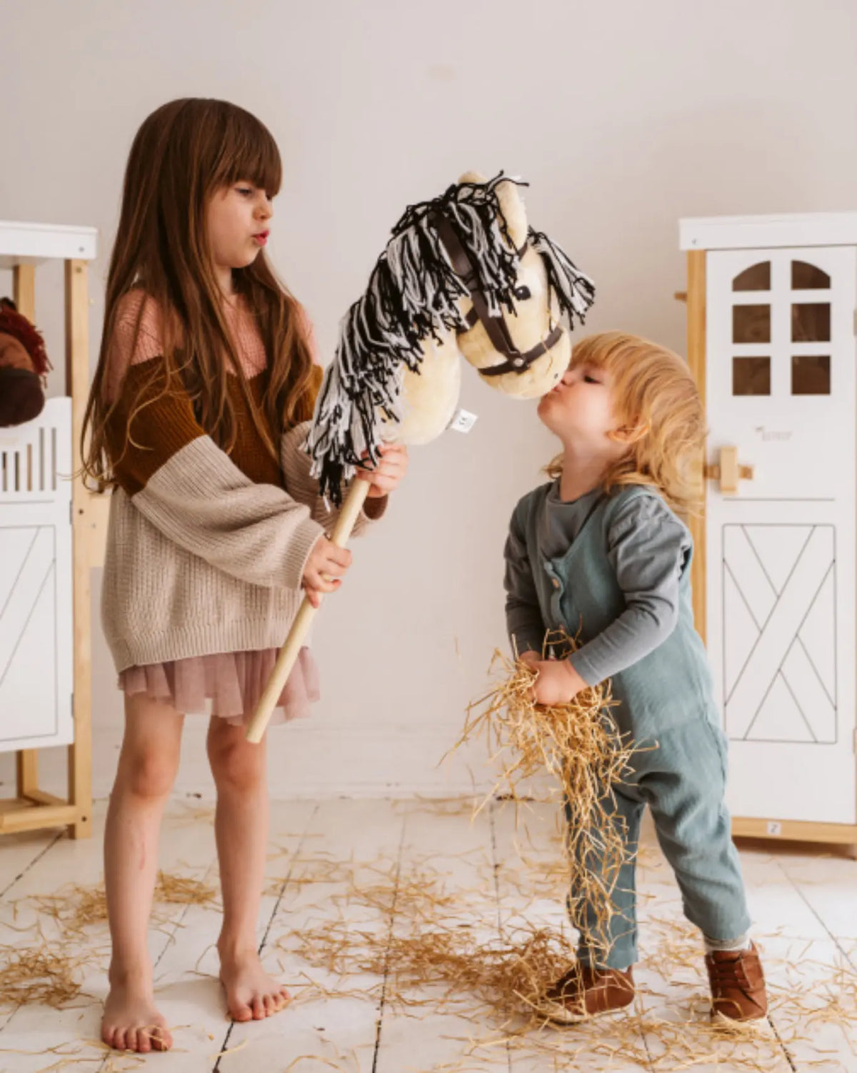 Zwei kleine Kinder spielen mit dem byASTRUP Hobby Horse Norweger; Mädchen hält das Steckenpferd, während das Kleinkind es streichelt.