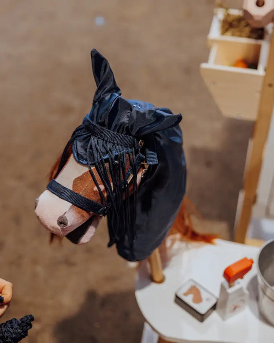 Nahaufnahme eines braunen Hobby Horses mit byASTRUP Regencape in Navy; praktisches Steckenpferd-Zubehör für Outdoor-Aktivitäten bei schlechtem Wetter.