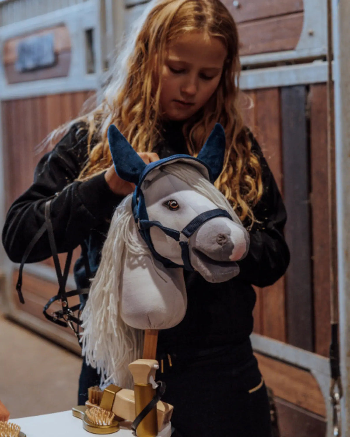 Kind zieht dem Hobby Horse die dunkelblaue Fliegenhaube von byASTRUP an; samtiges Turnierset für Steckenpferde.