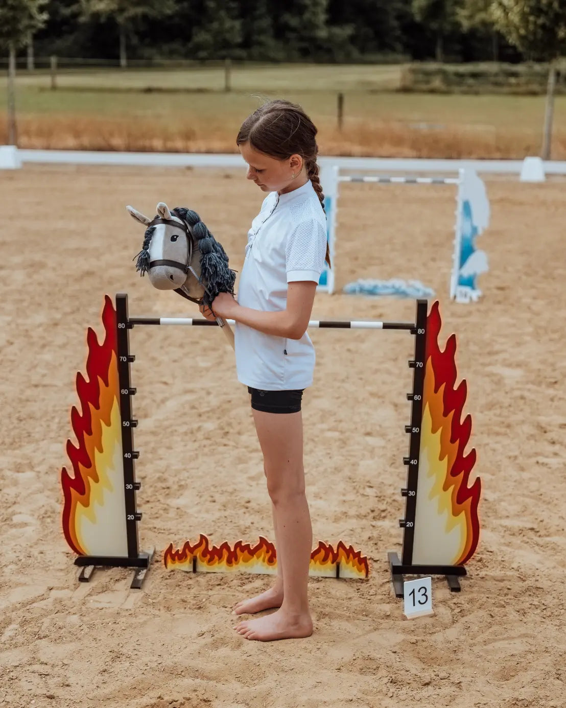 Hobby Horse Sprung mit verstellbarer Höhenskala bis 80 cm: Ein Mädchen misst die perfekte Sprunghöhe am feurigen byASTRUP Hindernis aus FSC-zertifiziertem Holz.