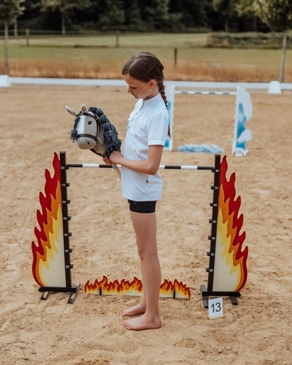 Hobby Horse Sprung mit verstellbarer Höhenskala bis 80 cm: Ein Mädchen misst die perfekte Sprunghöhe am feurigen byASTRUP Hindernis aus FSC-zertifiziertem Holz.