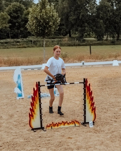 Effektives Koordinationstraining für kleine Turnierreiter: Kind reitet mit dem Steckenpferd auf das byASTRUP Fire-Hindernis zu – ideal zur Förderung von Kondition und Balance.