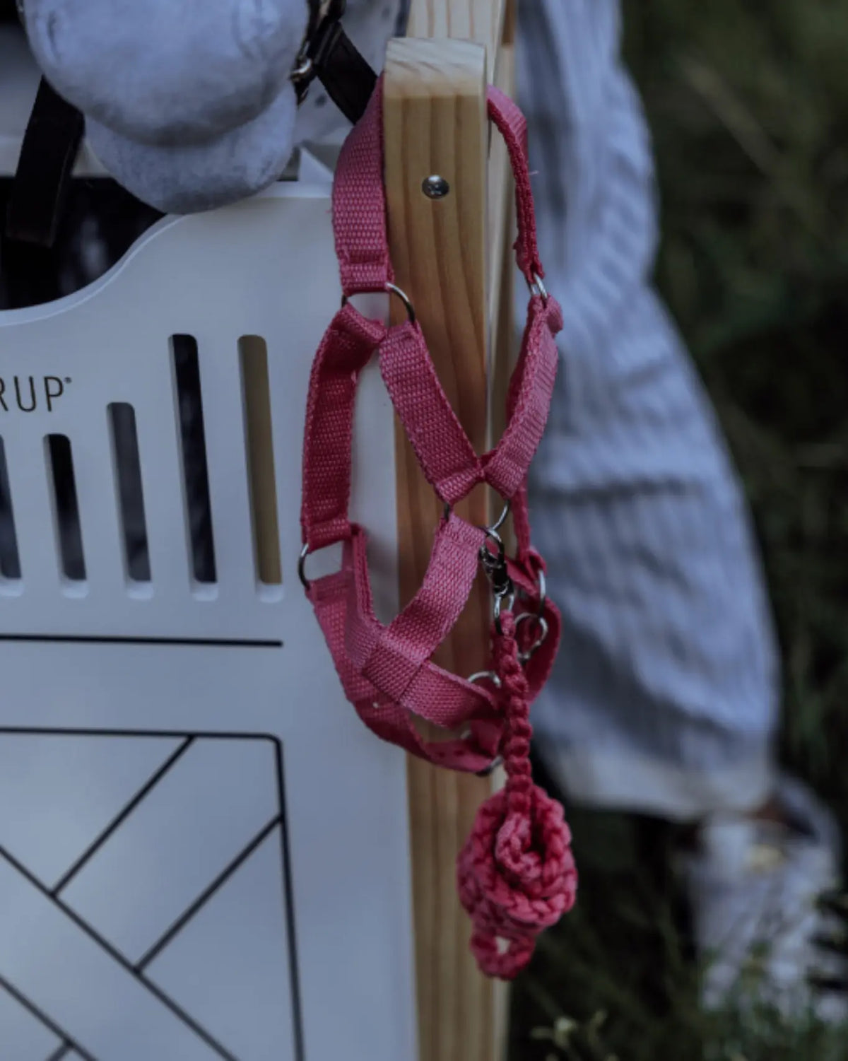 Pinkes byASTRUP Hobby Horse Halfter mit Strick hängt an einem weißen Holz-Stalltor im Freien; realistisches Zubehör für das Rollenspiel.