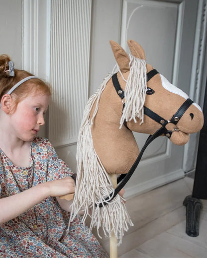 Fantasievolle Pferdepflege im Kinderzimmer: Ein Mädchen kämmt und stylt die lange weiße Mähne ihres hochwertigen byASTRUP Holz-Steckenpferds zur Förderung der Feinmotorik.