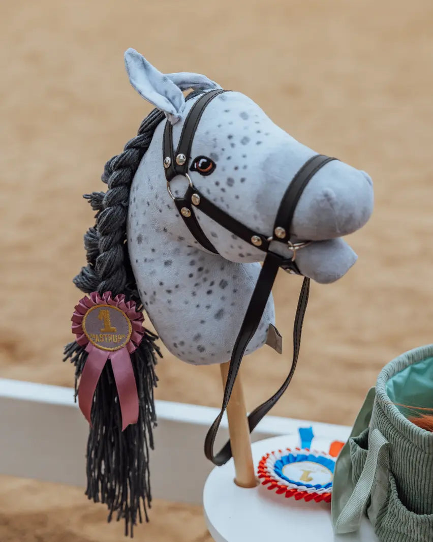 Hobby Horse Apfelschimmel ByAstrup in einer Reithalle mit Siegerschleife in der geflochtenen, grauen Mähne.