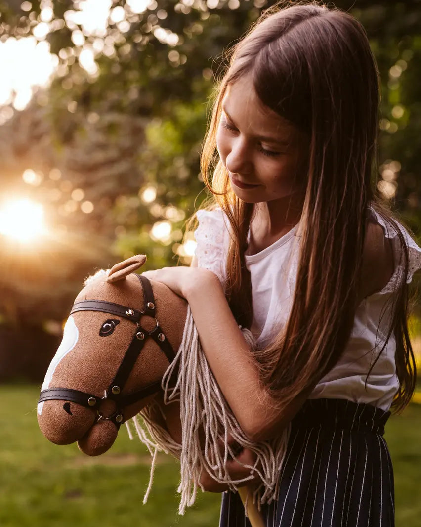 Lieblings-Kuscheltier und Steckenpferd: Ein Mädchen umarmt liebevoll ihr byASTRUP Hobby Horse Palomino im warmen Sonnenuntergang im Garten.