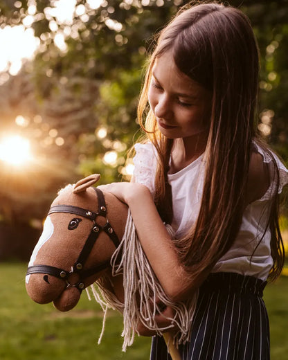 Lieblings-Kuscheltier und Steckenpferd: Ein Mädchen umarmt liebevoll ihr byASTRUP Hobby Horse Palomino im warmen Sonnenuntergang im Garten.