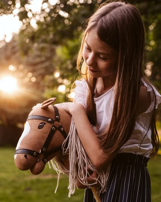Lieblings-Kuscheltier und Steckenpferd: Ein Mädchen umarmt liebevoll ihr byASTRUP Hobby Horse Palomino im warmen Sonnenuntergang im Garten.