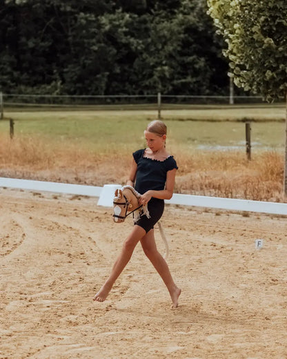 Hobby Horsing Parcours-Training: Ein Mädchen reitet barfuß mit dem beliebten byASTRUP Steckenpferd Palomino in Größe M auf einem sandigen Reitplatz.