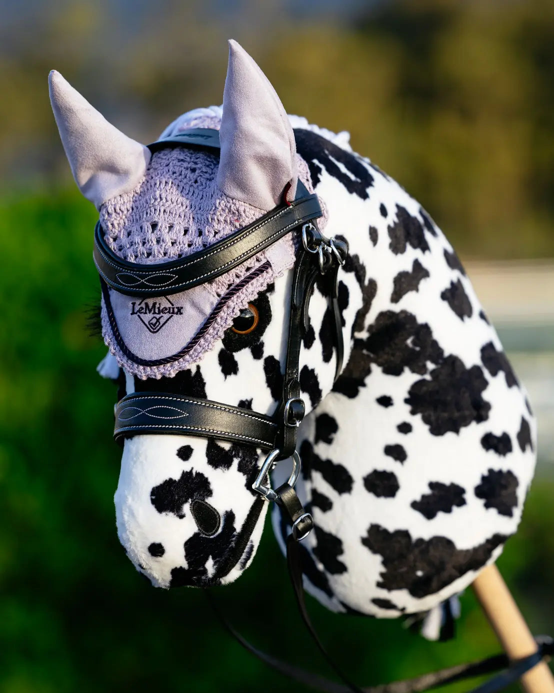 Professioneller Turnier-Look fürs Steckenpferd: Ein punktiertes Appaloosa Hobby Horse trägt die lila LeMieux Fliegenhaube passend zur Trense beim Outdoor-Training.