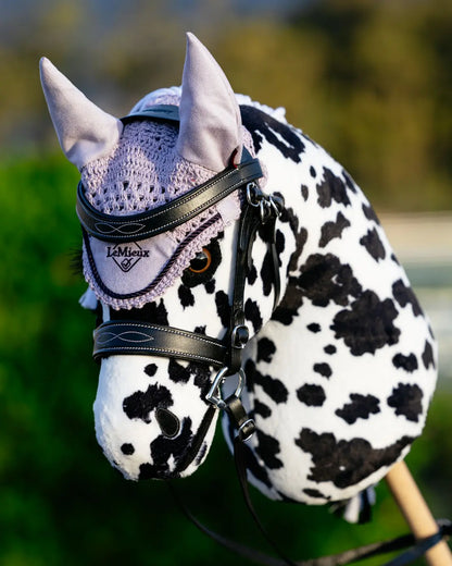 Professioneller Turnier-Look fürs Steckenpferd: Ein punktiertes Appaloosa Hobby Horse trägt die lila LeMieux Fliegenhaube passend zur Trense beim Outdoor-Training.