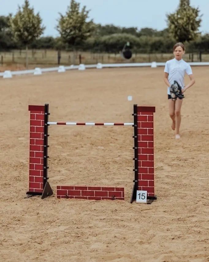 Hobby Horsing Parcours mit byASTRUP Hindernis in Backstein-Optik; im Hintergrund bereitet sich eine Hobby Horserin auf den Sprung vor