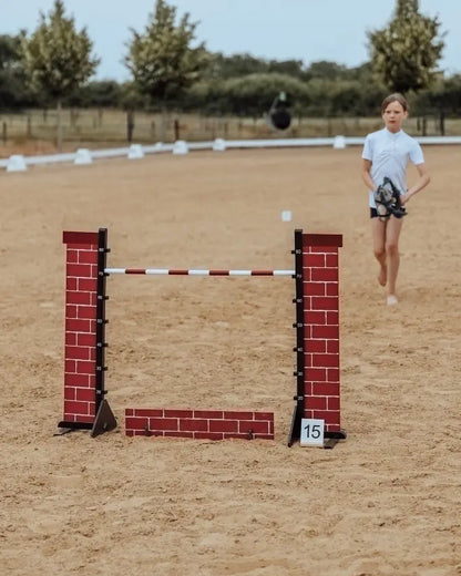 Hobby Horsing Parcours mit byASTRUP Hindernis in Backstein-Optik; im Hintergrund bereitet sich eine Hobby Horserin auf den Sprung vor