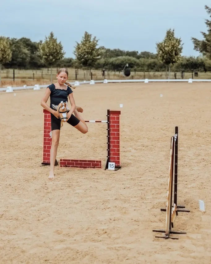 Seitenansicht eines byASTRUP Steckenpferd-Hindernisses auf Sandboden; Kind beim Hobby Horsing Dressur- und Springtraining