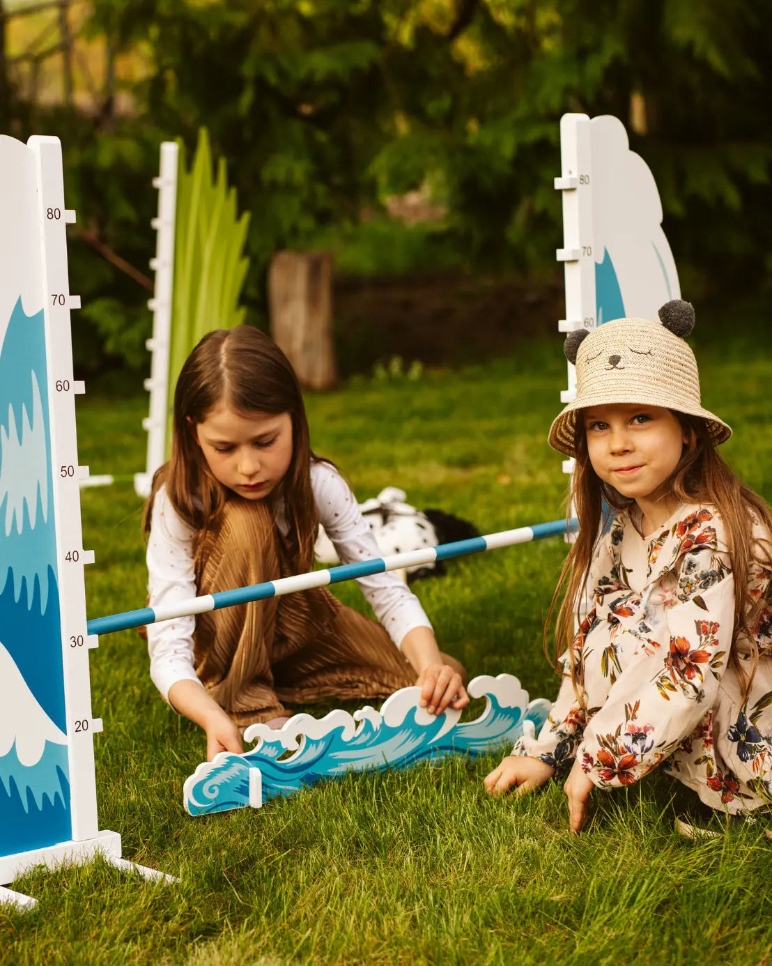 Detailansicht: Zwei Kinder verstellen die Höhe der Sprungstange am byASTRUP Hobby Horsing Hindernis im Garten.