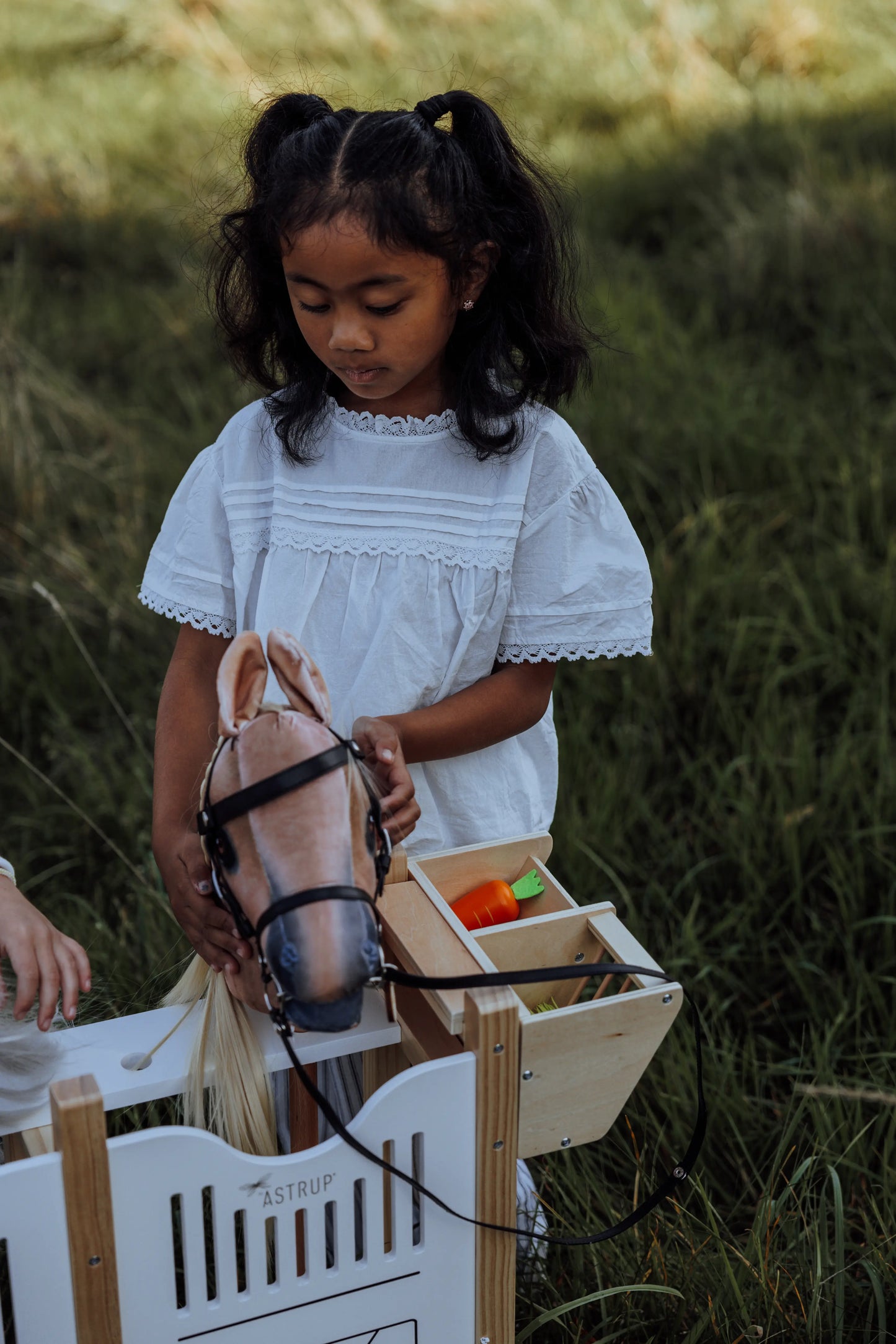 Kreatives Outdoorspiel mit dem byASTRUP: Ein Kind füttert ihr braunes Hobby Horse am abnehmbaren Trog der hochwertigen Holz hobby horse box.