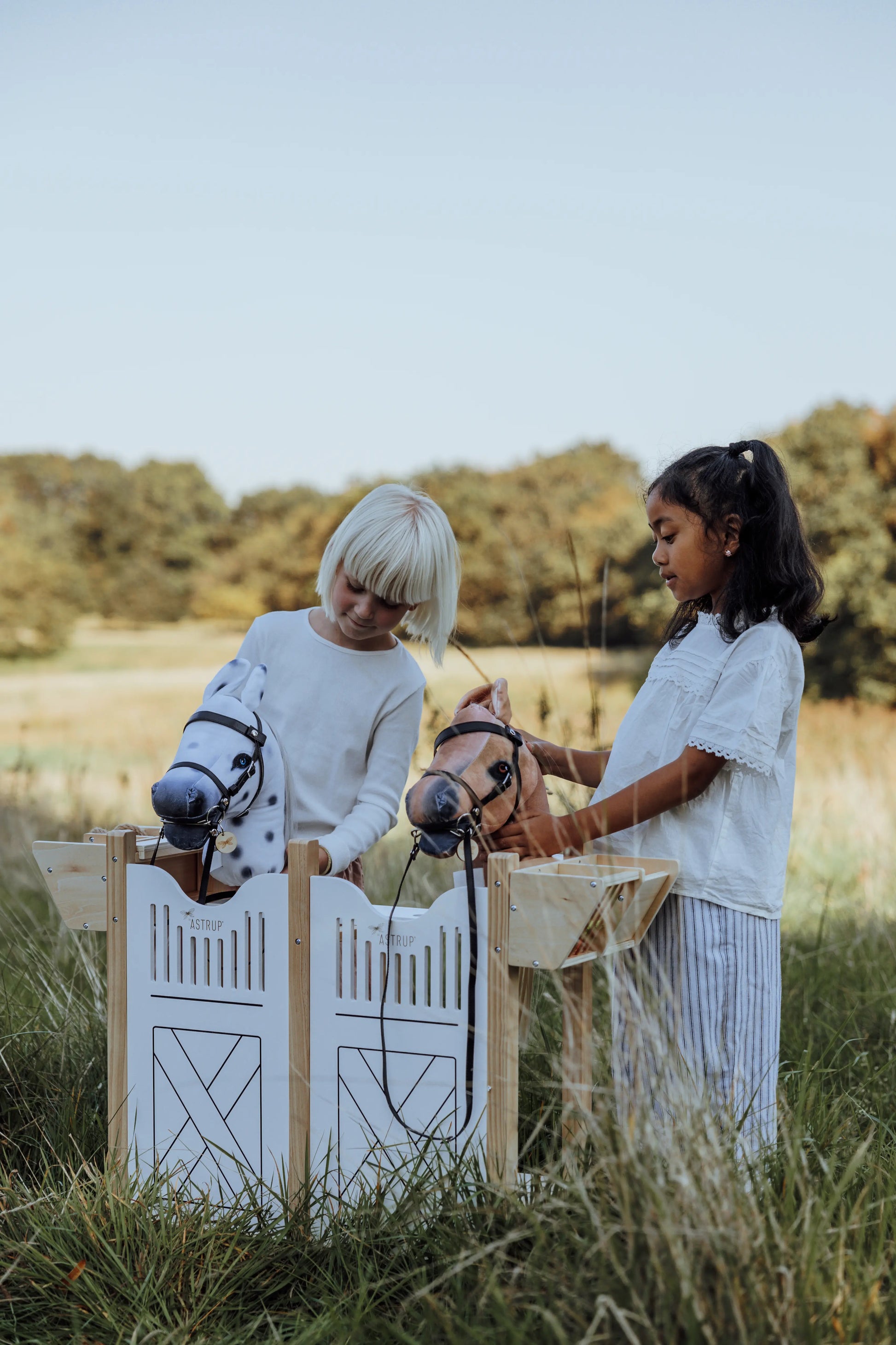 Premium Holzspielzeug für Pferdefans: Kinder versammeln sich um den großen byASTRUP Hobby Horse Stall für ein authentisches Reiterhof-Abenteuer an der frischen Luft.