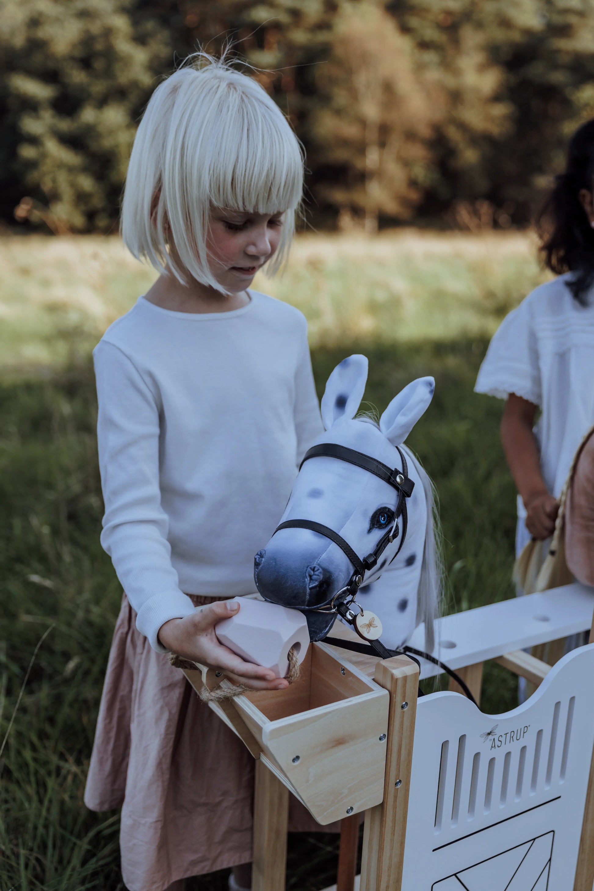 Realistisches Hobby Horsing Zubehör bei lope.de: Kind nutzt den integrierten Futtertrog des byASTRUP Stalls, um das Steckenpferd spielerisch zu versorgen.