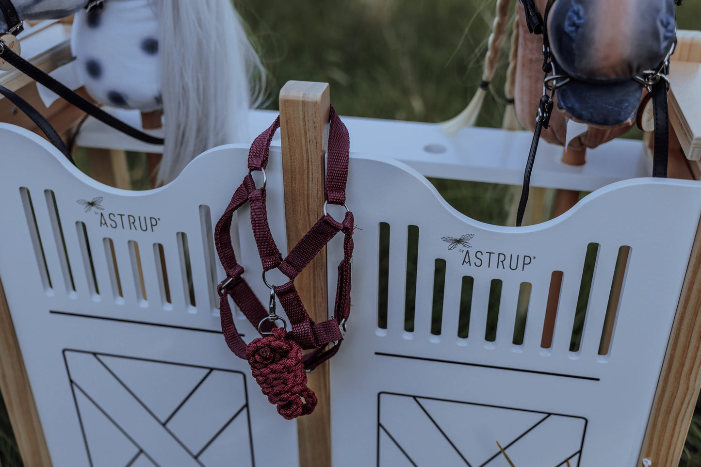 Ein rotes Steckenpferd-Halfter hängt griffbereit am byASTRUP Hobby horse stall aus robustem Holz in Weiß und Natur.
