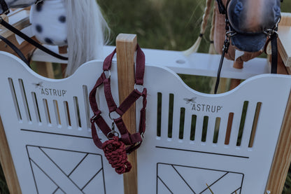 Ein rotes Steckenpferd-Halfter hängt griffbereit am byASTRUP Hobby horse stall aus robustem Holz in Weiß und Natur.