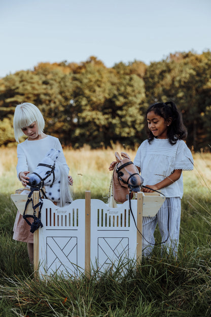Zwei Kinder spielen gemeinsam auf einer Wiese mit der ByAstrup Box für vier Hobby Horses – ein Highlight für das kreative Rollenspiel.