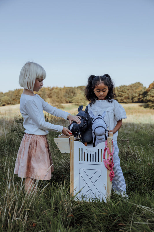 Kinder versammeln sich um den byASTRUP Hobby Horse Stall auf einer Koppel für ein realistisches Rollenspiel.