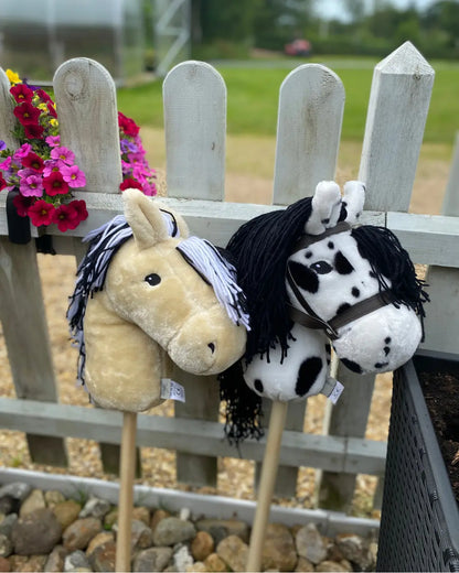 Hochwertige byASTRUP Hobby Horses am Zaun: Ein beiges und ein weiß-schwarz punktiertes Steckenpferd ideal für das Hobby Horsing im Freien.