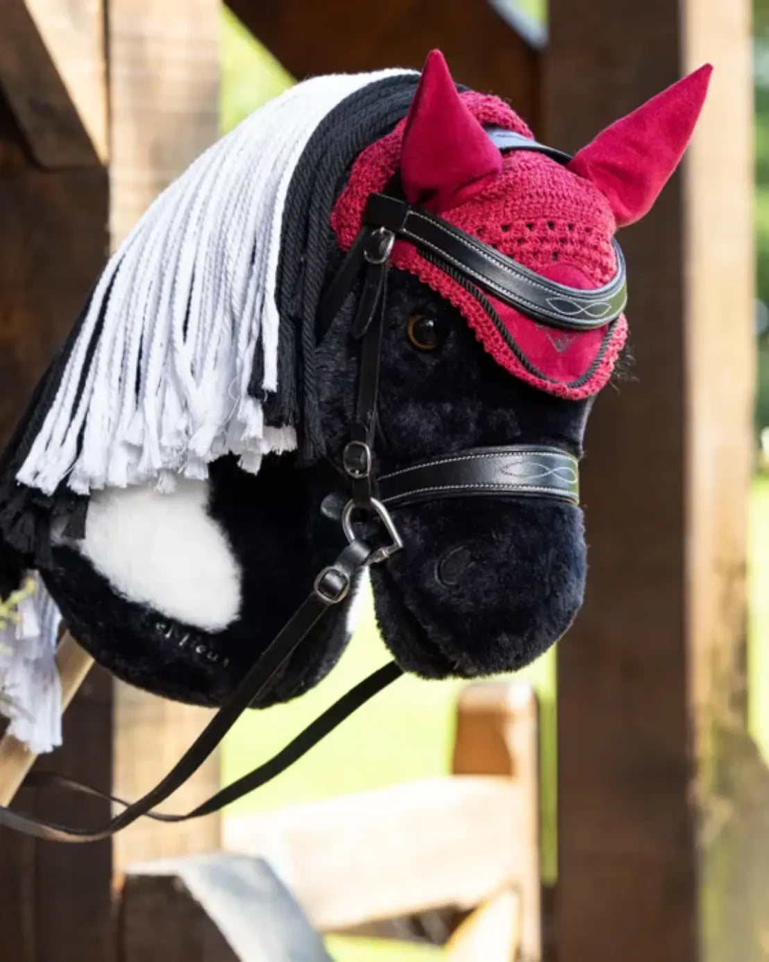 lemieux hobby horse fliegenhaube auf einem schwarz weiß geschecktem lemieux hobby horse, dass aus einem stall schaut und eine schwarze hobby horse trense trägt.