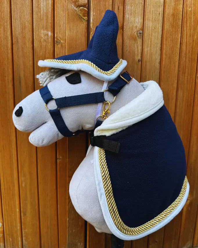 panduro hobby horse set mit hobby horse paradedecke mit goldkordel an einem grauen hobby horse vor einer holzwand