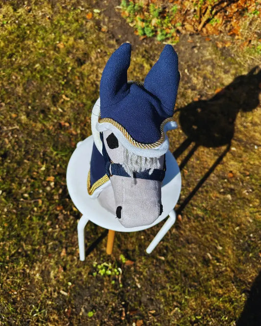 hochwertiges panduro hobby horse set aus einer dunkelblauem fleece hobby horse paradedecke, einem dunkelblauem hobby horse halfter und einer dunkelblauen fleece fliegenhaube mit goldkordel an einem grauen hobby horse aus der vogelperspektive