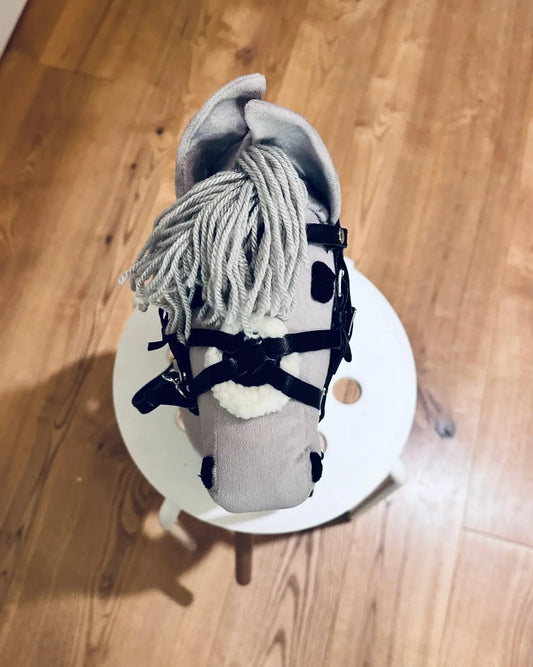 Aufnahme eines finnischen, hellgrauen Hobby Horses, dass eine schwarze Panduro Hobby Horse Trense trägt. Die Trense hat ein Reithalfter im mexikanischem Stil und ist weich unterlegt.